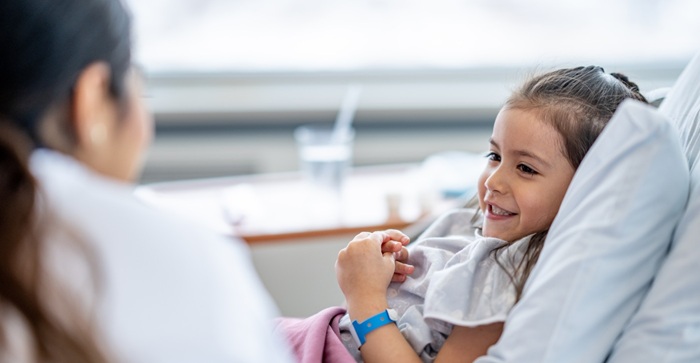 female nurse checks on a pediatric patient post-surgery, who is tucked in and in good spirits.